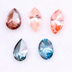 Collection of fancy color lab grown diamonds including pink marquise cut, light peach marquise, brown pear shape, blue oval cut and blue pear cut loose diamonds displayed on white background