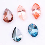 Collection of fancy color lab grown diamonds including pink marquise cut, light peach marquise, brown pear shape, blue oval cut and blue pear cut loose diamonds displayed on white background