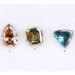 Three fancy color lab grown diamonds including pear cut pink diamond, asscher cut olive diamond, and trillion cut blue diamond displayed on white background for custom jewelry making