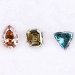 Three fancy color lab grown diamonds including pear cut pink diamond, asscher cut olive diamond, and trillion cut blue diamond displayed on white background for custom jewelry making