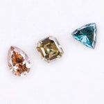 Three fancy color lab grown diamonds including pear cut pink diamond, asscher cut olive diamond, and trillion cut blue diamond displayed on white background for custom jewelry making