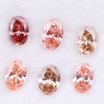 Six oval cut pink lab grown diamonds in varying shades from vivid rose and blush pink to soft peach and champagne, displayed on a white background, showcasing brilliant faceting and exceptional sparkle.