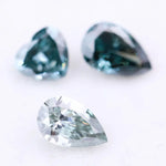 Three blue lab grown diamonds displayed on white background: pear cut light blue diamond (1), heart cut teal diamond (2), and deep blue pear shaped diamond (3), brilliant faceted loose stones for engagement ring or custom fine jewelry.