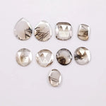 Assorted rose cut lab grown diamonds with natural-looking inclusions in oval, pear, round and cushion shapes arranged on white background for fine jewelry design.