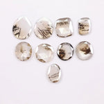 Assorted rose cut lab grown diamonds with natural-looking inclusions in oval, pear, round and cushion shapes arranged on white background for fine jewelry design.