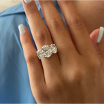 Three-stone oval diamond engagement ring in white gold on a woman’s hand with light blue manicure