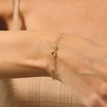 Gold bracelet with heart charms on a wrist against a neutral background