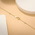 Gold bracelet with heart charms on a wrist against a neutral background