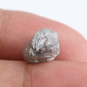 A rough, raw diamond held between metal tweezers against a clean white background.