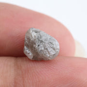 A rough, raw diamond held between metal tweezers against a clean white background.