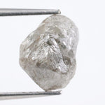 A rough, raw diamond held between metal tweezers against a clean white background.