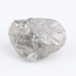 A rough, raw diamond held between metal tweezers against a clean white background.