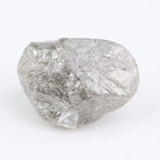 A rough, raw diamond held between metal tweezers against a clean white background.