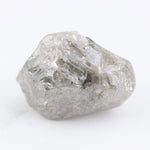 A rough, raw diamond held between metal tweezers against a clean white background.