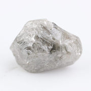A rough, raw diamond held between metal tweezers against a clean white background.