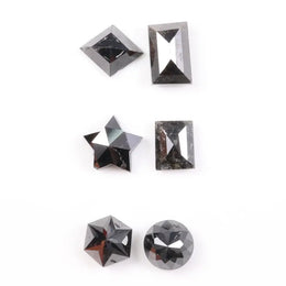 Six natural black diamonds in geometric cuts including star, kite, emerald rectangle, pentagon, and round brilliant shapes displayed on white background.
