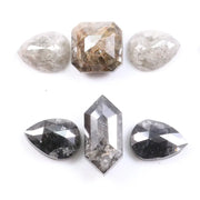 Assorted natural salt and pepper and white rustic diamonds in pear, hexagon, and elongated geometric cuts displayed on a white background, featuring visible inclusions and raw organic patterns.