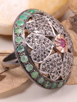 Silver ring with green gemstones and a pink stone on a beige background