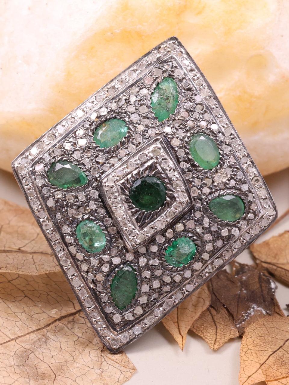 Silver ring with green gemstones on a beige background with leaves