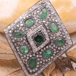 Silver ring with green gemstones on a beige background with leaves