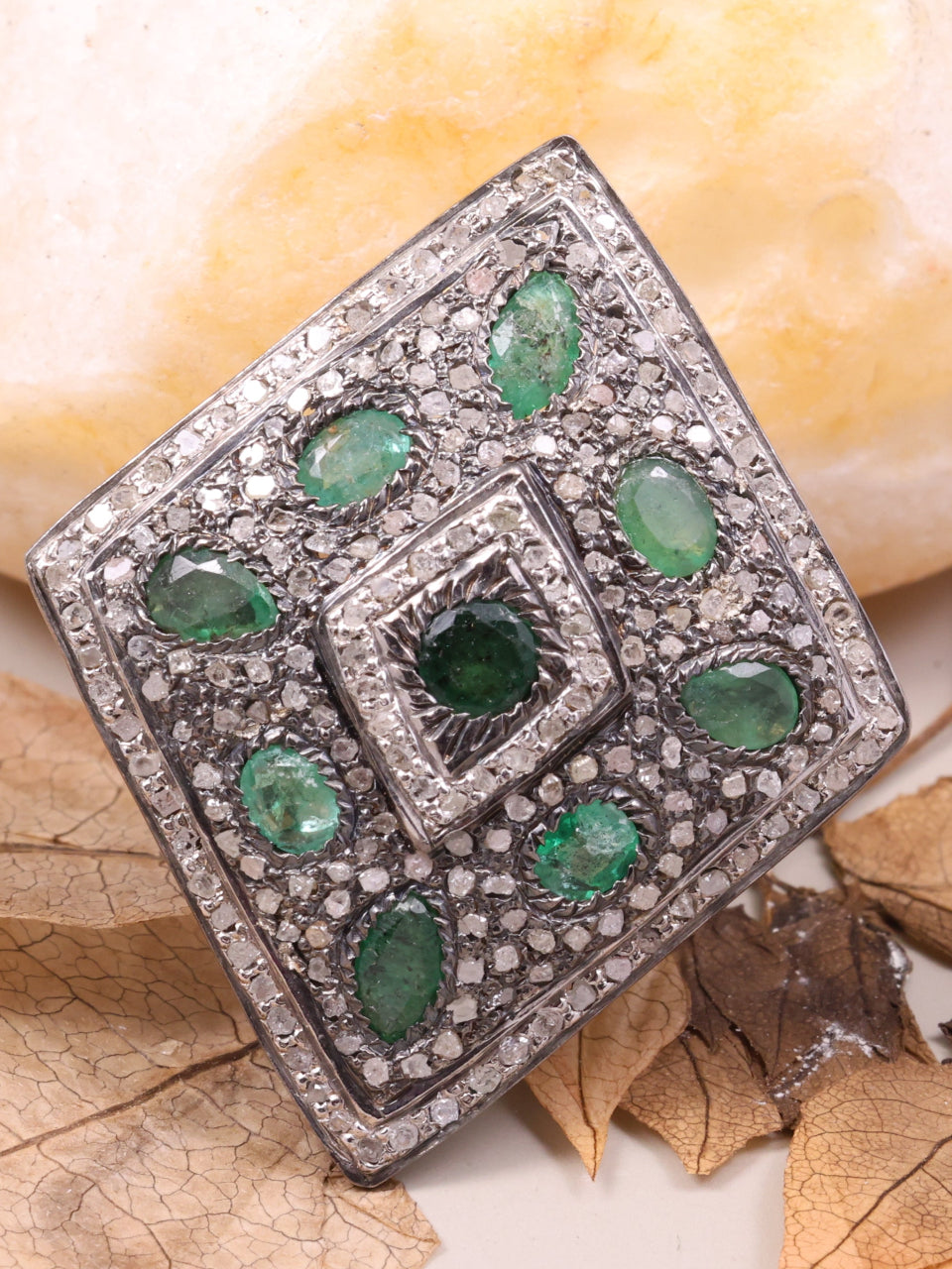 Silver brooch with green gemstones on a stone and leaves background