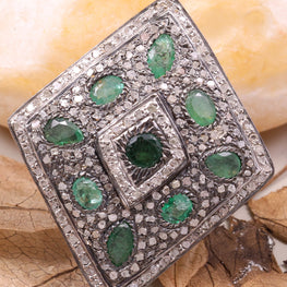 Silver brooch with green gemstones on a stone and leaves background