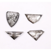 Four salt and pepper lab grown diamonds in shield, trillion, and geometric fancy cuts with natural grey inclusions, displayed on white background as loose ethical conflict-free stones for custom jewelry.