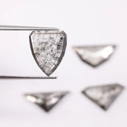 Four salt and pepper lab grown diamonds in shield, trillion, and geometric fancy cuts with natural grey inclusions, displayed on white background as loose ethical conflict-free stones for custom jewelry.