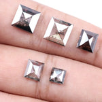 Five square step-cut lab grown diamonds with pyramid-style faceting and visible natural inclusions displayed on a white background, featuring clear, salt and pepper, and champagne tones.