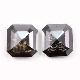 Pair of emerald cut salt and pepper lab grown diamonds with black and white inclusions in geometric step cut, shown loose on white background.