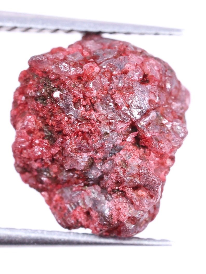 Raw red diamond held by tweezers on a white background