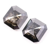 Pair of emerald cut salt and pepper lab grown diamonds with black and white inclusions in geometric step cut, shown loose on white background.