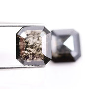 Pair of emerald cut salt and pepper lab grown diamonds with black and white inclusions in geometric step cut, shown loose on white background.