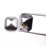 Pair of emerald cut salt and pepper lab grown diamonds with black and white inclusions in geometric step cut, shown loose on white background.