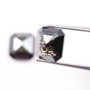 Pair of emerald cut salt and pepper lab grown diamonds with black and white inclusions in geometric step cut, shown loose on white background.