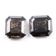 Pair of emerald cut salt and pepper lab grown diamonds with black and white inclusions in geometric step cut, shown loose on white background.