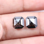 Pair of emerald cut salt and pepper lab grown diamonds with black and white inclusions in geometric step cut, shown loose on white background.