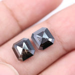 Pair of emerald cut salt and pepper lab grown diamonds with black and white inclusions in geometric step cut, shown loose on white background.