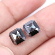 Pair of emerald cut salt and pepper lab grown diamonds with black and white inclusions in geometric step cut, shown loose on white background.