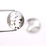 Two round brilliant cut lab grown diamonds with black galaxy-style inclusions on white background, faceted loose stones for custom fine jewelry.