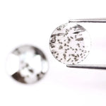 Two round brilliant cut lab grown diamonds with black galaxy-style inclusions on white background, faceted loose stones for custom fine jewelry.