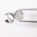 Two round brilliant cut lab grown diamonds with black galaxy-style inclusions on white background, faceted loose stones for custom fine jewelry.