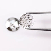 Two round brilliant cut lab grown diamonds with black galaxy-style inclusions on white background, faceted loose stones for custom fine jewelry.