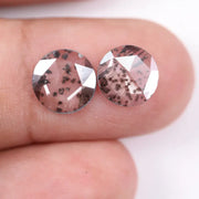 Two round brilliant cut lab grown diamonds with black galaxy-style inclusions on white background, faceted loose stones for custom fine jewelry.