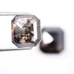 Emerald cut lab grown salt and pepper diamond with geometric step cut facets featuring bold black and smoky inclusions, octagonal shape, ethical sustainable gemstone.