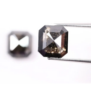 Emerald cut lab grown salt and pepper diamond with geometric step cut facets featuring bold black and smoky inclusions, octagonal shape, ethical sustainable gemstone.