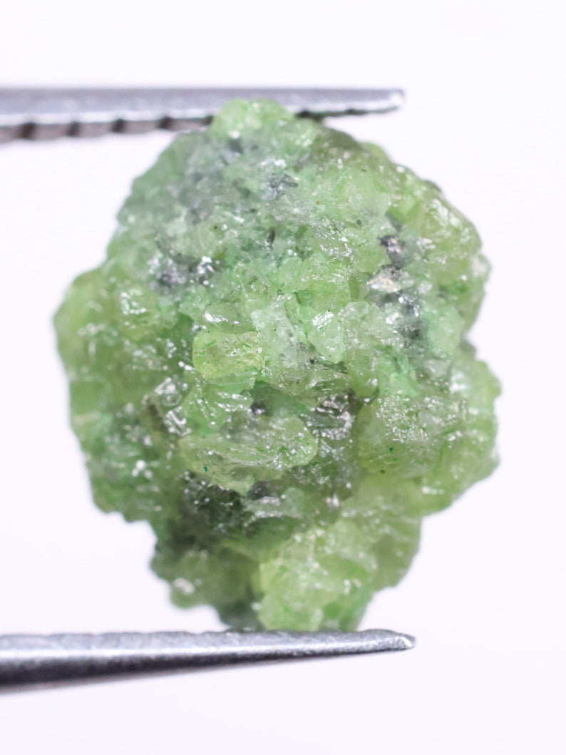 Green diamond held by tweezers on a white background