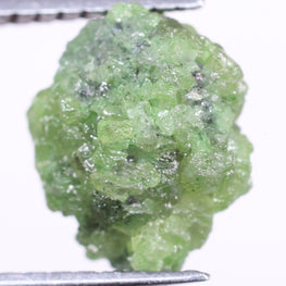 Green diamond held by tweezers on a white background