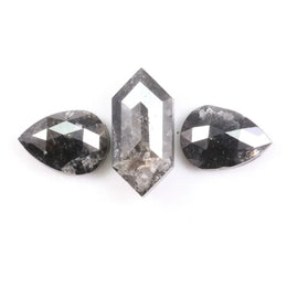 Three natural salt and pepper diamonds including a kite cut center stone and two pear shaped side stones with grey inclusions and rose cut faceting on a white background.