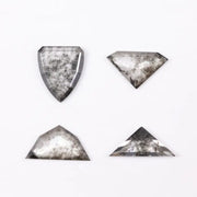 Four salt and pepper lab grown diamonds in shield, trillion, and geometric fancy cuts with natural grey inclusions, displayed on white background as loose ethical conflict-free stones for custom jewelry.